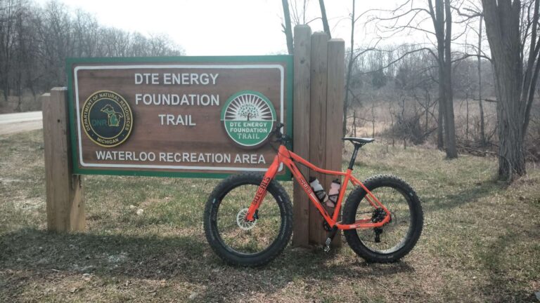 orange fat tire bike leaning against a trail sign