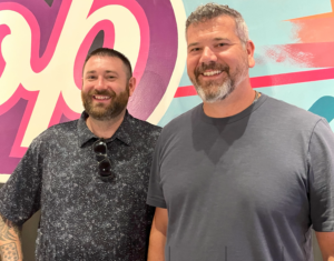 Two men in front of colorful sign