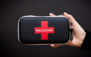 Hand holding red and black case of Naloxone
