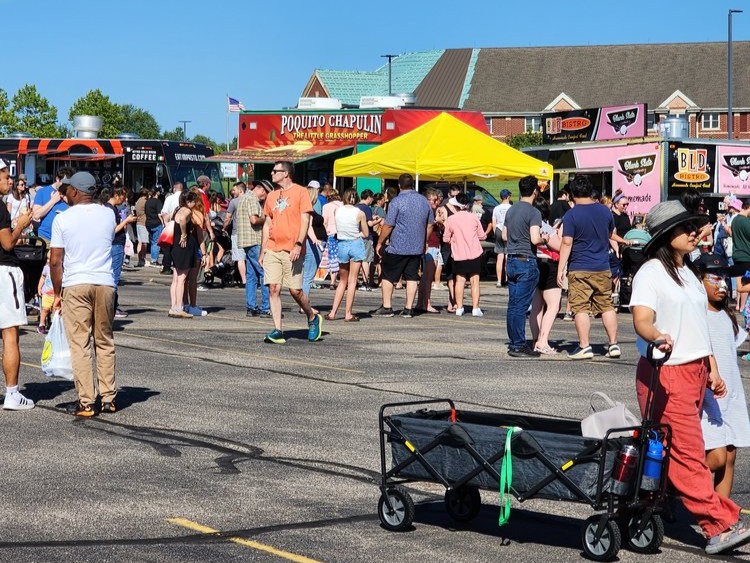 Crowds enjoying food trucks at the Saline Food Truck Festival with kids playing and classic cars on display