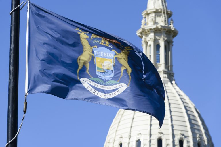 Michigan flag waving in front of the beautiful dome of the Capitol